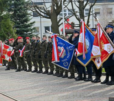 Dwór. Na chodniku stoją salutujący żołnierze ze sztandarami pochylonymi do przodu