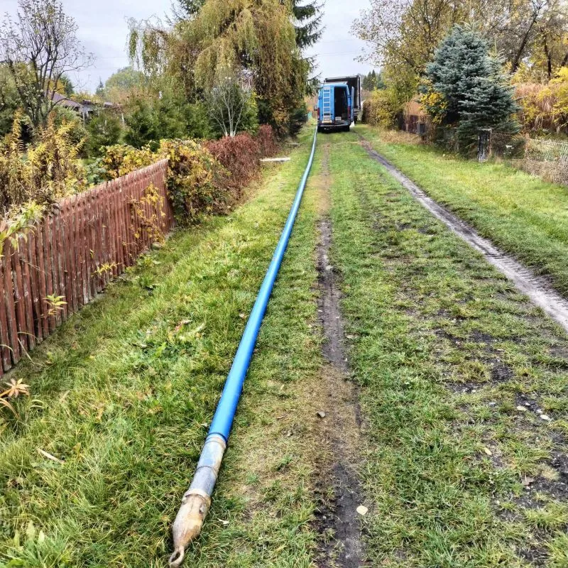 Niebieska rura rozciągnięta wzdłuż trawiastej drogi prowadzącej do zaparkowanego vana.