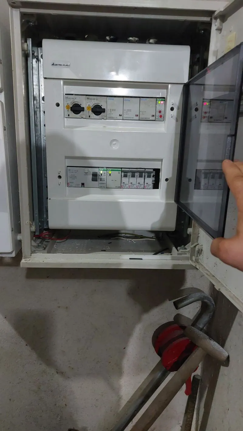 Biała rozdzielnia elektryczna z włączonymi bezpiecznikami i otwartymi przezroczystymi drzwiami.