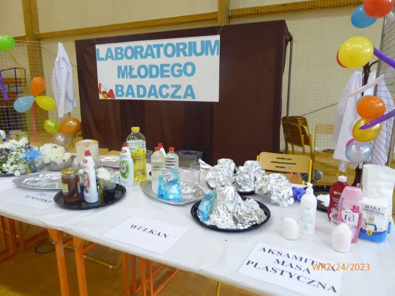 Stół z zestawem produktów chemicznych i składników do doświadczeń pod tablicą z napisem „Laboratorium Młodego Badacza”.