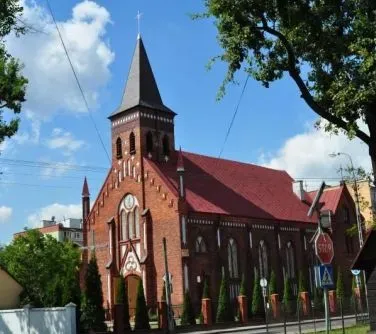 Ceglana neogotycka świątynia z wysoką strzelistą wieżą i czerwonym dachem.