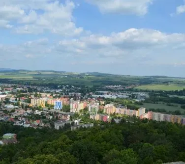 Zespół kolorowych bloków mieszkalnych otoczonych terenami zielonymi i rozległym krajobrazem wiejskim w tle.