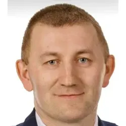 Głowa mężczyzny o jasnej karnacji, krótkich jasnobrązowych włosach i niebieskich oczach, ubrany w garnitur.