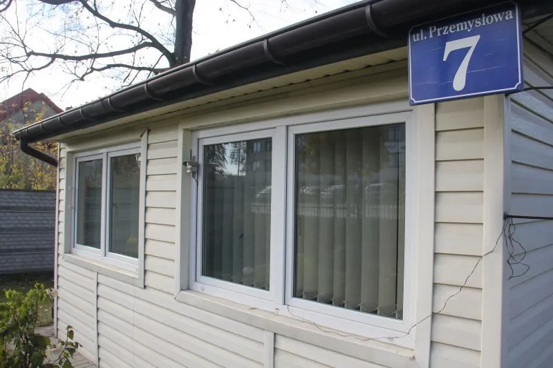 Biały budynek z trzema oknami i niebieską tabliczką adresową z napisem "ul. Przemysłowa 7".
