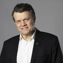 Mężczyzna w średnim wieku w białej koszuli i ciemnej marynarce na szarym tle.