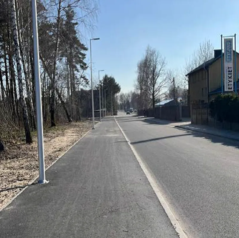 Pusta ulica z chodnikiem, latarniami i budynkiem z reklamą po prawej stronie.