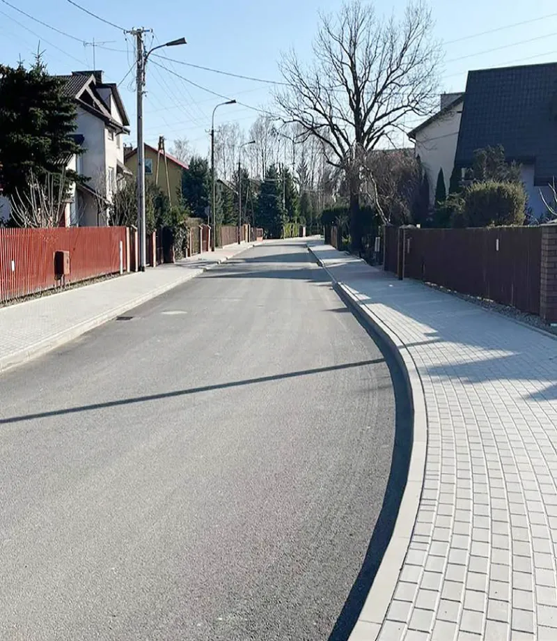 Pusty asfaltowy chodnik z kostki brukowej i ogrodzenia przydomowych działek po obu stronach ulicy.