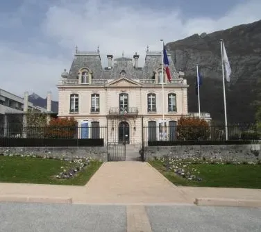 Dwupiętrowy budynek o klasycznej architekturze z kilkoma flagami ustawionymi przed wejściem.