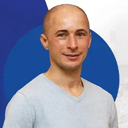 Mężczyzna o łysiejącej głowie w jasnoszarej koszulce na niebieskim i białym tle.