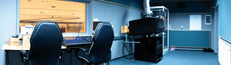 Pomieszczenie studyjne z biurkiem, sprzętem audio i dwoma czarnymi krzesłami.