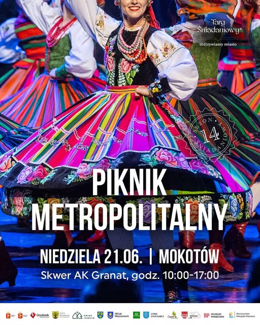 Kliknięcie powiększy obraz. Grupa tancerek w kolorowych, tradycyjnych strojach ludowych wiruje na scenie. Skoncentrowane ujęcie pokazuje gorsety i szerokie, wielobarwne spódnice z kwiatowymi haftami. Jedna tancerka z uśmiechem trzyma ręce na biodrze. Tło ciemne; na obrazie widoczny jasny napis promocyjny i pasek z logotypami organizatorów.