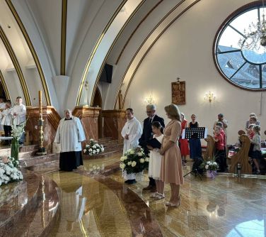 wnętrze kościoła przed ołtarzem z prawej strony dziewczynka mówi do mikrofonu obok niej kobieta i mężczyzna