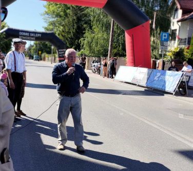 Na dworze. Mężczyzna przemawia do mikrofonu stojąc na ulicy. W tle dmuchany nad ulicą czarno-czerwony balon