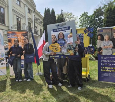 Na dworze. nastolatki rozbią sobie zdjęcie w ramce europejskiej. Po lewej stoją dwie nastolatki między banerami. W tle pałac