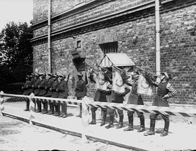 Czarno-białe zdjęcie. Szpaler żołnierzy z karabinami. Obok czterech żołnierzy dmących w trąbki