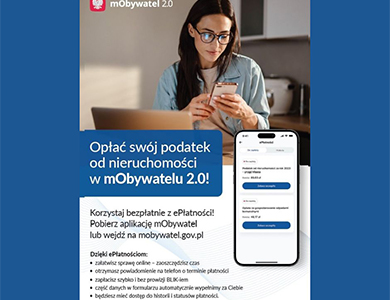 Kobieta z ciemnymi długimi włosami i okularach siedzi przed laptopem. Patrzy w telefon